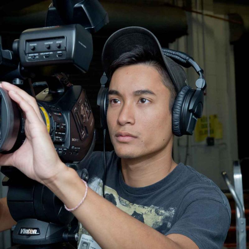 A person operates a camera while wearing a headset.