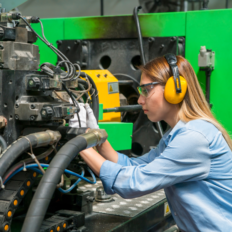 An engineer in protective hearing and vision equipment works on a machine