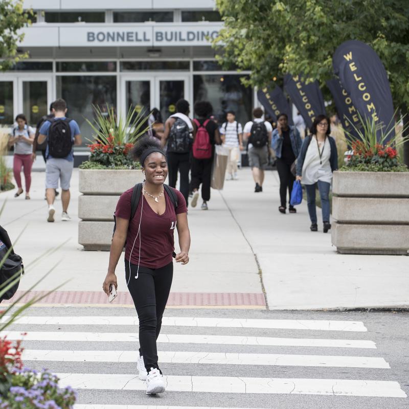 Smiling student walks across a busy campus.