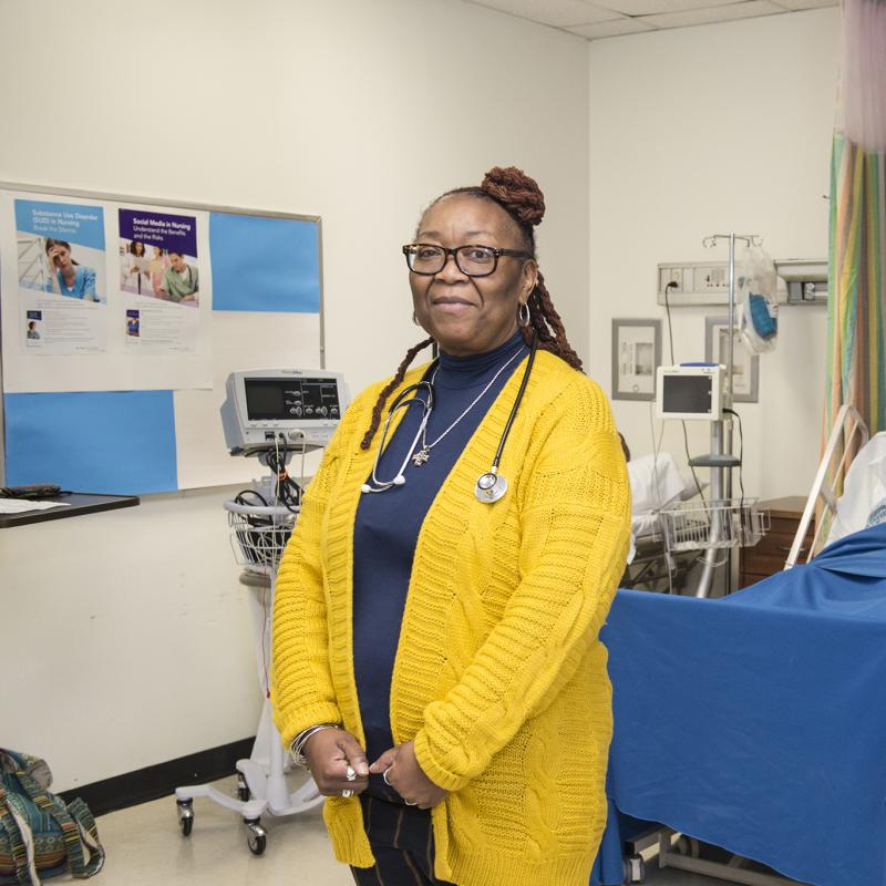 A woman with a stethoscope in a hospital room smiles for the camera.