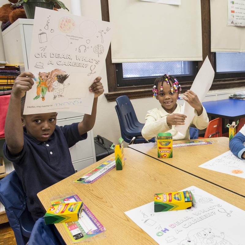 Children in a classroom hold up their coloring.