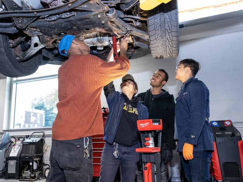 Four students work under a truck on a lift.