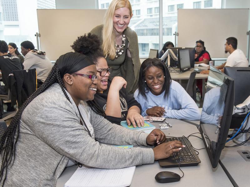 Instructor and three students at a computer laugh.