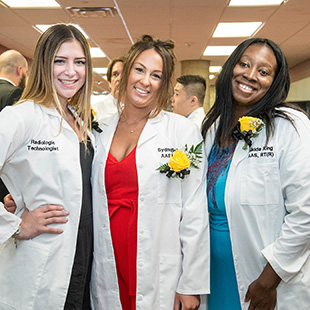 3 nursing students standing together smiling during their graduation 