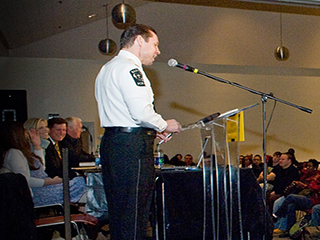 Presentation froma member of the police. uniformed presenter facing a crowd of people, presenting from a podium.