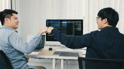 Two people smiling and fist bumping while coding together