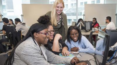 Instructor and three students at a computer laugh.