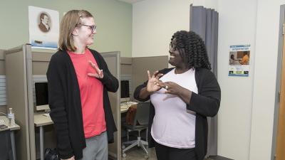 two students smiling and communicating in American Sign Language (ASL)