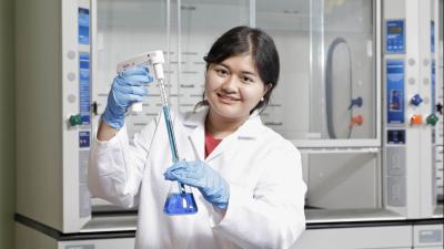 smiling student wearing a lab coat working in the biology lab