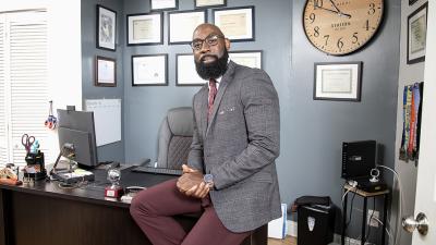 Smiling Philadelphia business owner sits on desk in his office
