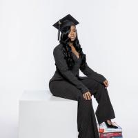 Ash jones's graduation photoshoot. She's wearing a black pinstripes pantsuit and a graduation cap. 