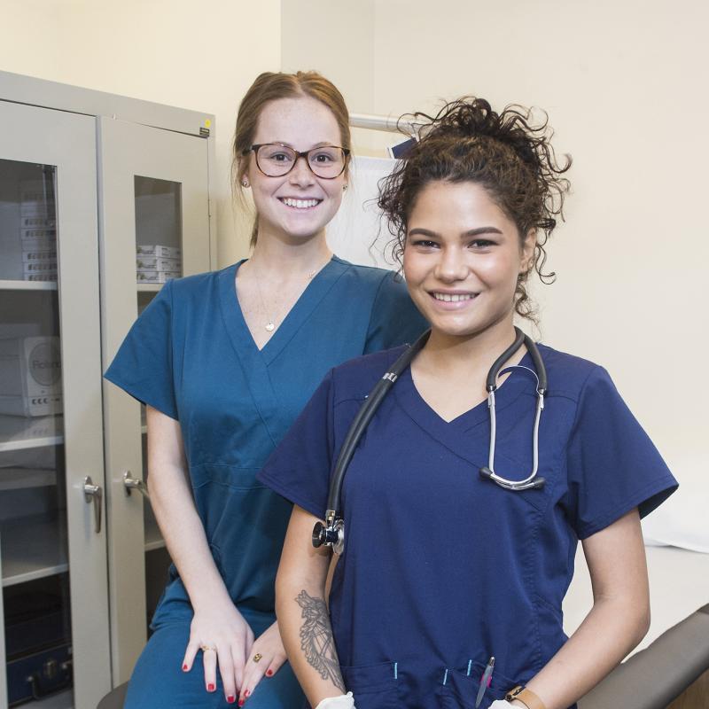 Two students in scrubs smile for the camera.