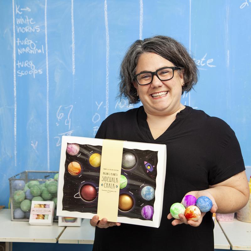Business owner holds colorful chalk products.