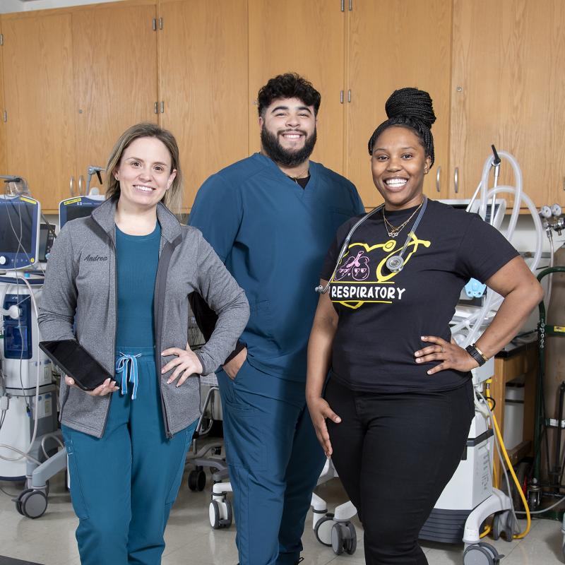 Three respiratory therapy students pose for the camera in a classroom.