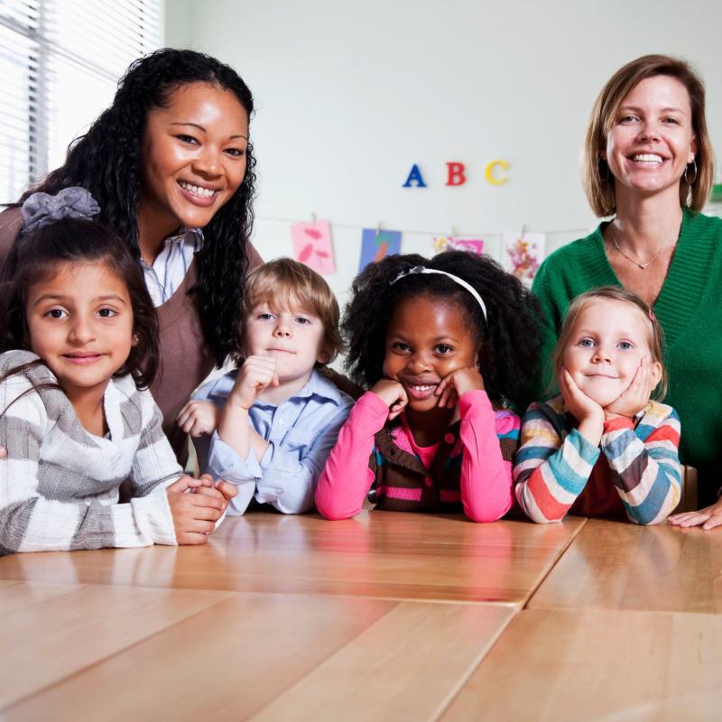 Two preschool teachers smiling with a group of students