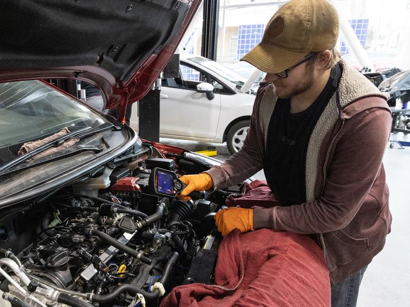 Student uses diagnostic tool over car engine.