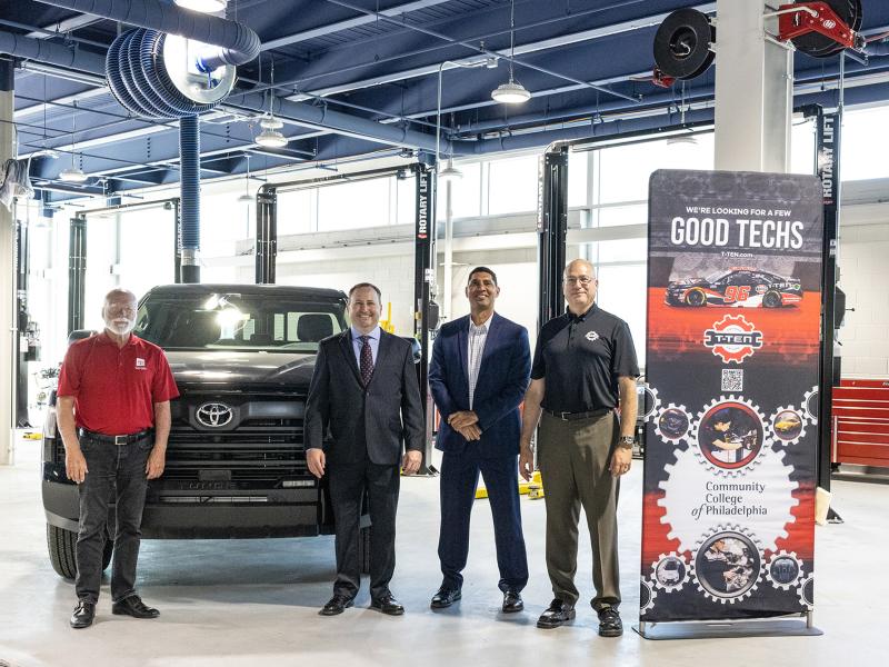 A group stands in a modern automotive garage in front of a truck and next to a banner.