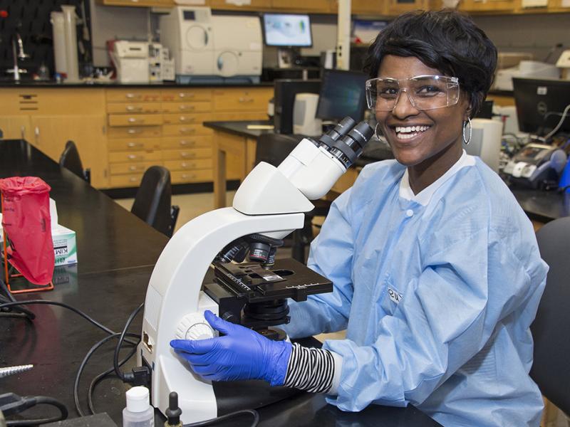 A smiling medical lab technologist seated at a microscope
