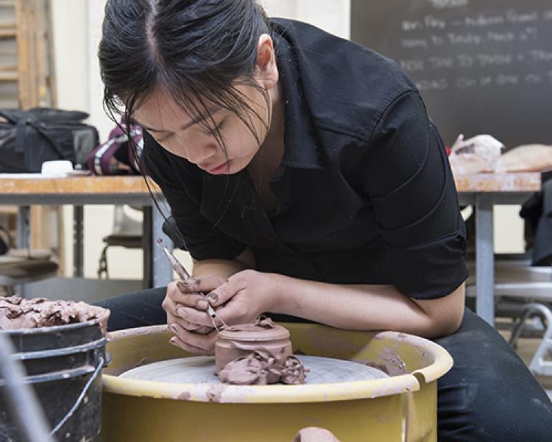 student throwing clay at pottery wheel