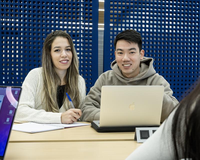 Two students working in the library using a laptop and notebook