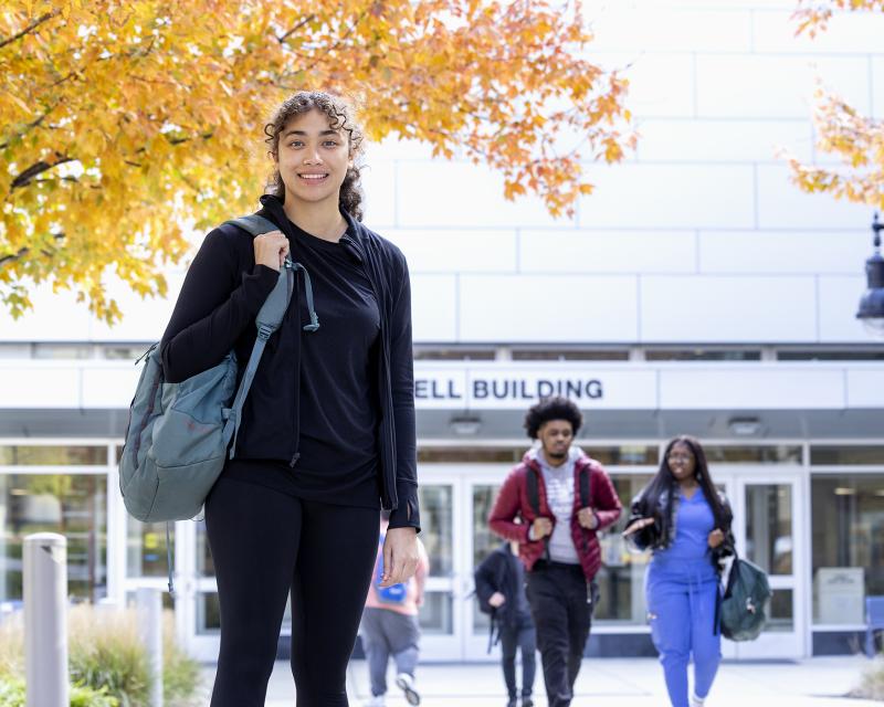 Student standing on campus with fall leaves in the background