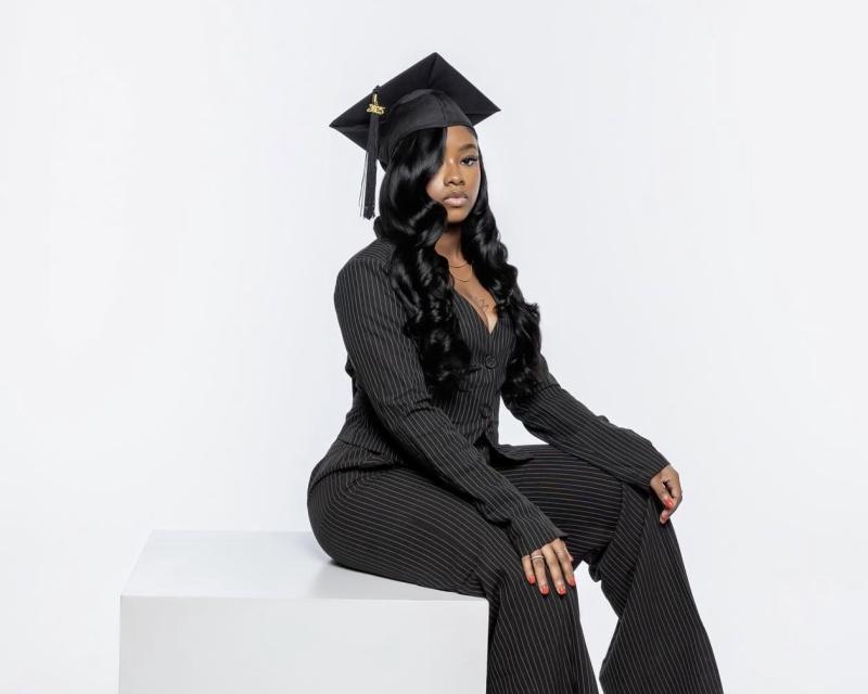 Ash jones's graduation photoshoot. She's wearing a black pinstripes pantsuit and a graduation cap. 