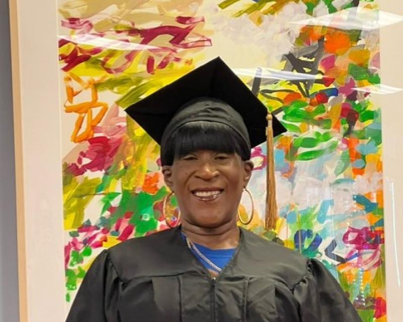 Tracey Downing in her graduation gown posing with two thumbs up